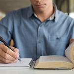 man with book writing on pad